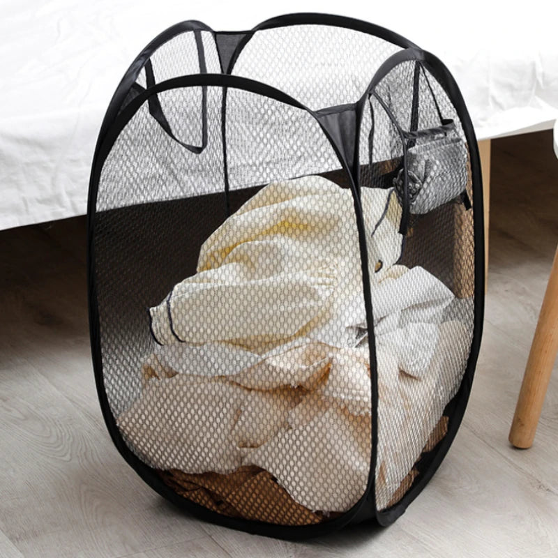 Black collapsible mesh laundry basket with side pockets filled with white laundry