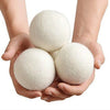 Two hands are holding several white reusable wool dryer balls.
