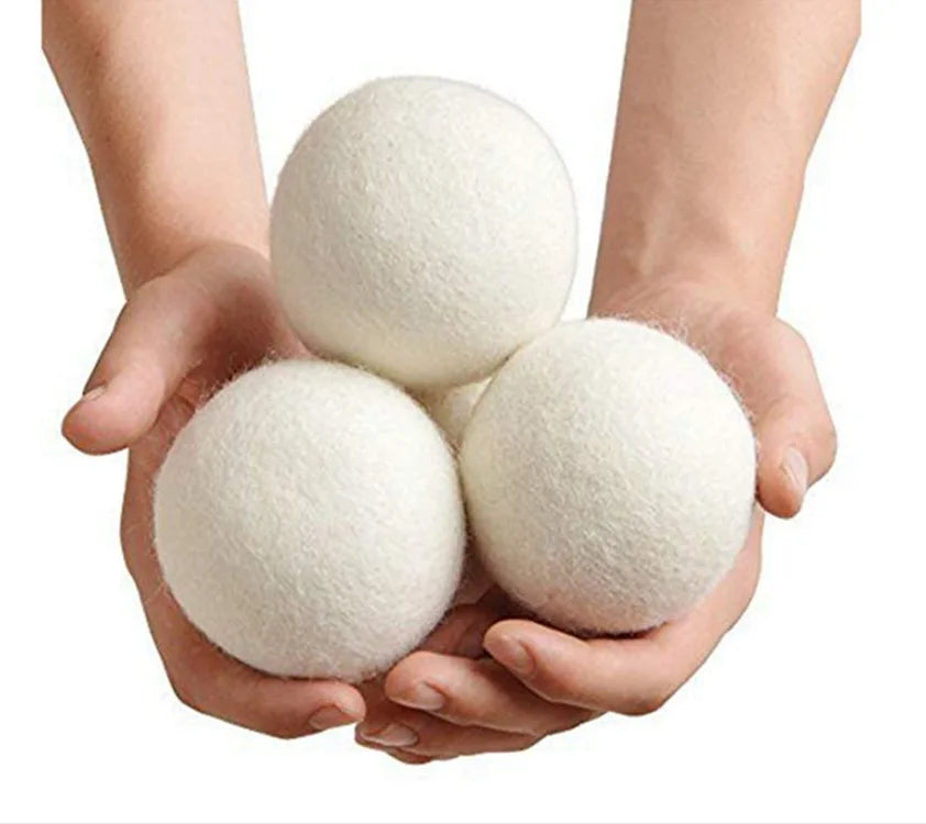 Two hands are holding several white reusable wool dryer balls.