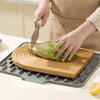 A hand is using a knife to cut a piece of lettuce on a wooden cutting board placed on a silicone drain mat.