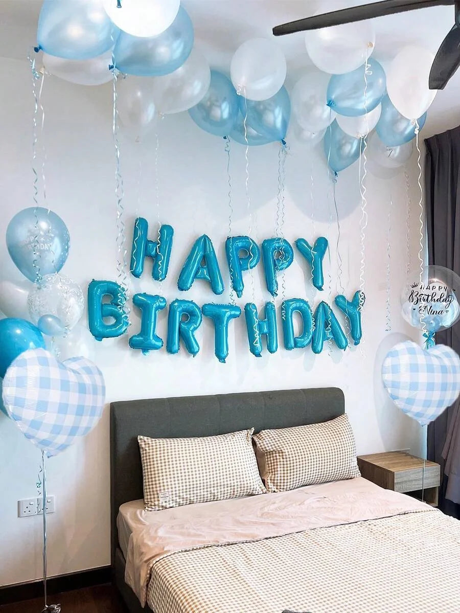 A wall decorated with blue and white balloons spelling out Happy Birthday above a bed.