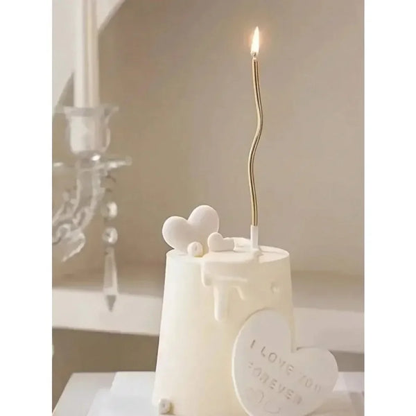 A white decorative candle holder with a lit gold spiral candle and a heart-shaped tag that reads I love you forever