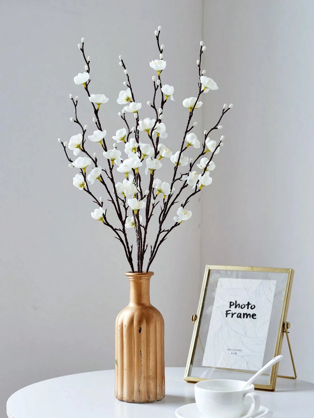 Eine Vase hält einen Zweig künstlicher weißer Pflaumenblüten vor hellem Hintergrund.