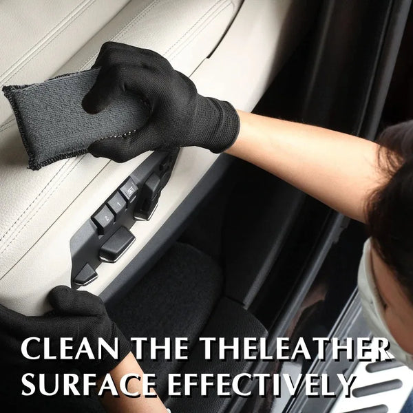 A hand wearing a black glove cleans the leather surface of a car interior with a scrubbing sponge.