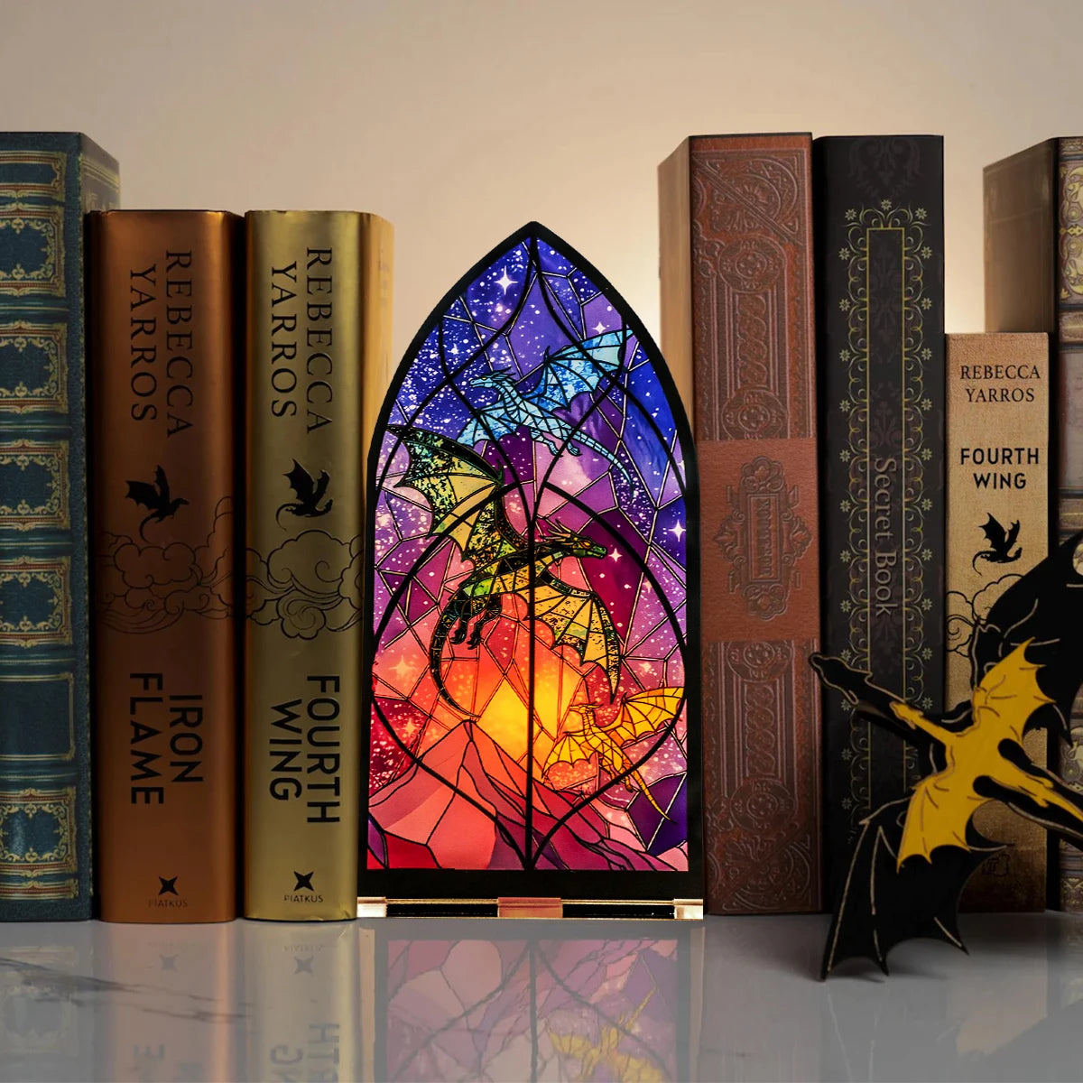 Un juego de cuatro libros encuadernados en cuero y un candelabro de dragón gótico con detalles de vidrieras de colores.