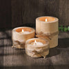 Tres troncos de madera natural envueltos con cuerda sirven como portavelas para decoración.