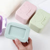 Three ceramic soap dishes with lids in pink, mint green, and light blue are shown on a white surface.