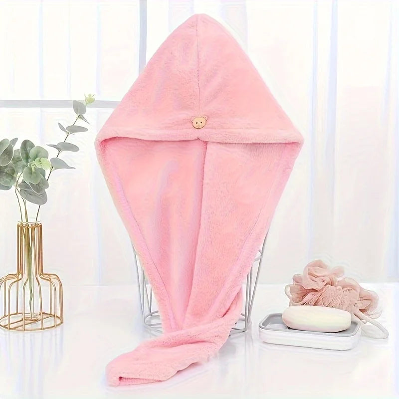 A pink microfiber hair drying wrap towel displayed on a clear stand next to a plant.