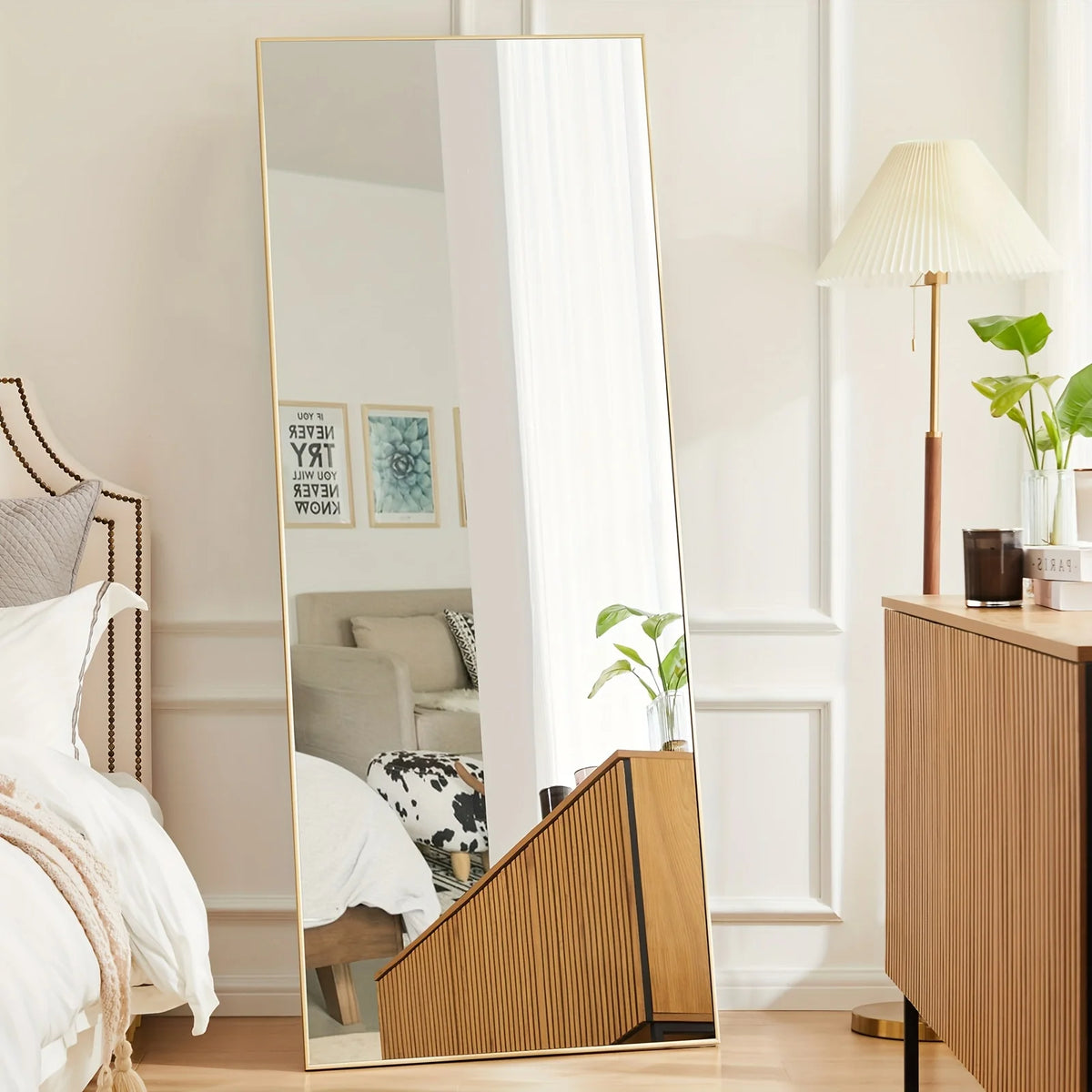 A full length arch mirror with a gold aluminum frame reflecting a bright interior and a potted plant.
