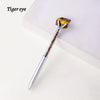 A silver pen with a natural yellow-orange crystal tip resembling a tiger eye is displayed on a white surface.