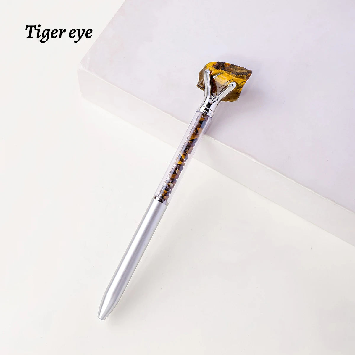 A silver pen with a natural yellow-orange crystal tip resembling a tiger eye is displayed on a white surface.