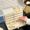 A hand is placing a pearl necklace into a white acrylic 5-tier desktop jewelry organizer rack.