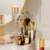 A clear, spherical rotating organizer for makeup brushes with gold accents and a lid, shown on a white surface.