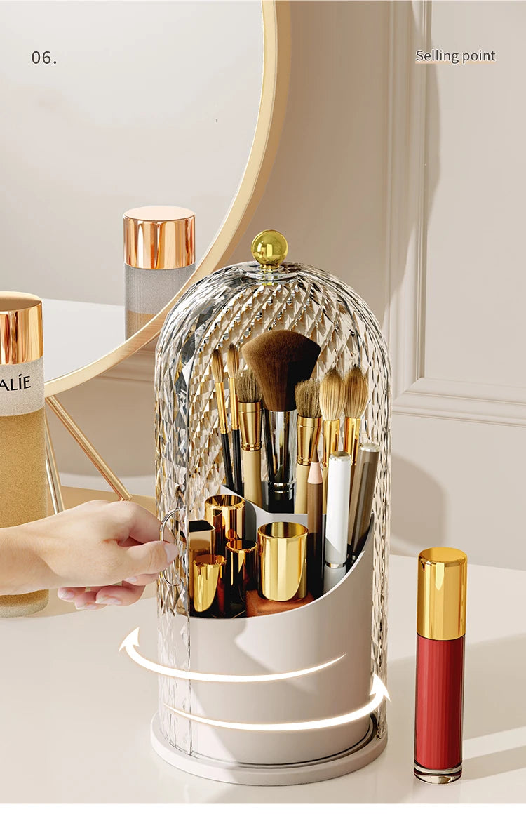 A clear, spherical rotating organizer for makeup brushes with gold accents and a lid, shown on a white surface.