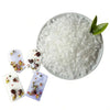 Material granular blanco para hacer velas, mostrado en un cuenco junto a pequeñas piezas decorativas de cera.