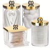 A clear glass apothecary jar dispenser for cotton balls and swabs with a golden lid.