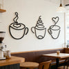 Un juego de tres piezas decorativas de tazas de café de hierro negro exhibidas en una pared blanca sobre un banco de madera.