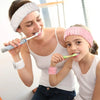 A woman is brushing a child's teeth with a toothbrush while the child wears a pink headband.