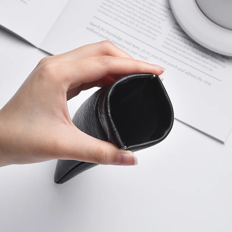A hand holds a black PU leather squeeze eyeglasses case with soft lining next to a piece of paper.