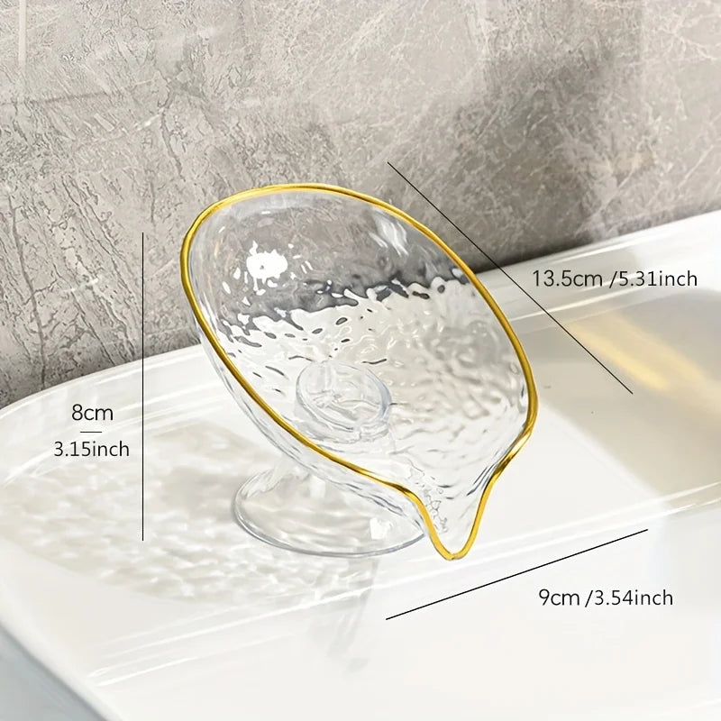 Clear oval plastic soap dish with a gold rim and drainage holes shown on a white surface.