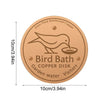 A round copper disk bird bath for garden water with a silhouette of a bird on it.