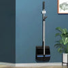 A long handle broom and dustpan set with a black and silver design against a blue wall.