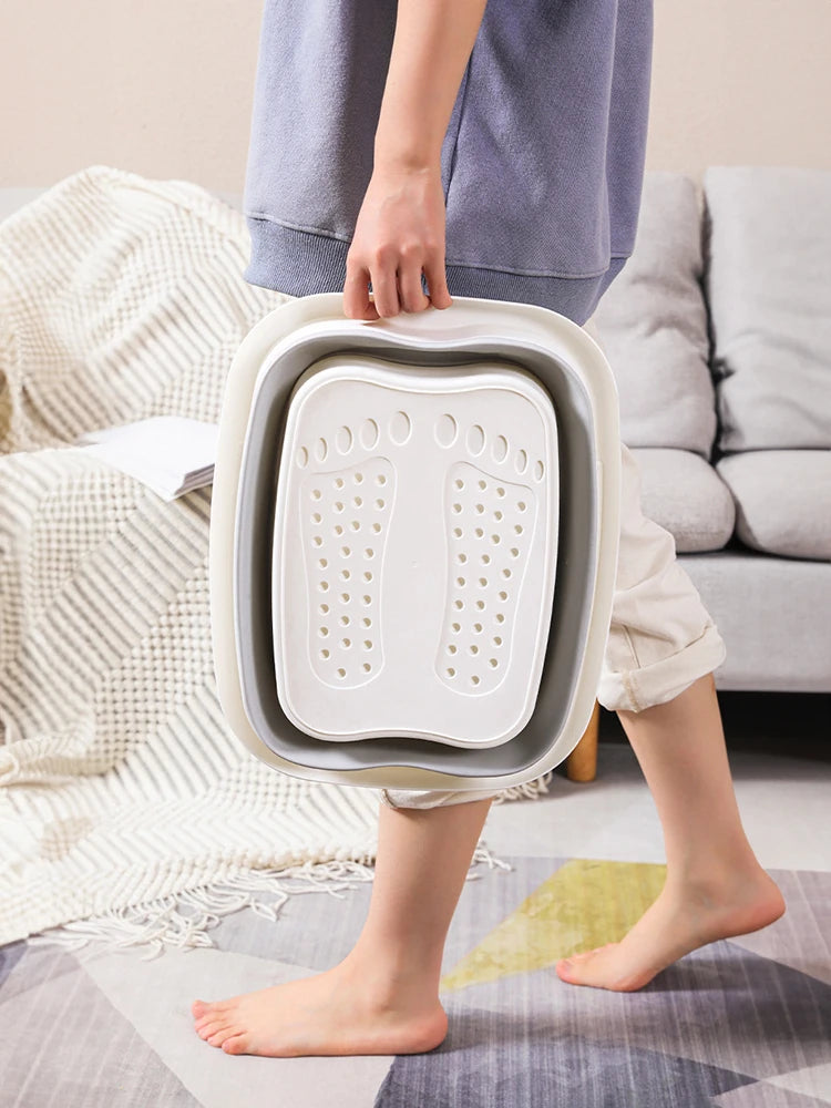 A person holds a white foldable foot soak bucket for therapeutic massage.