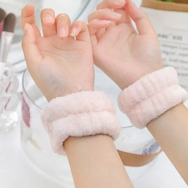 A pair of pink microfiber wrist sweatbands for face washing and skincare are shown on hands.
