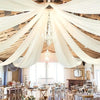 A wedding or event venue with a high ceiling draped in sheer white chiffon fabric and featuring a crystal chandelier.