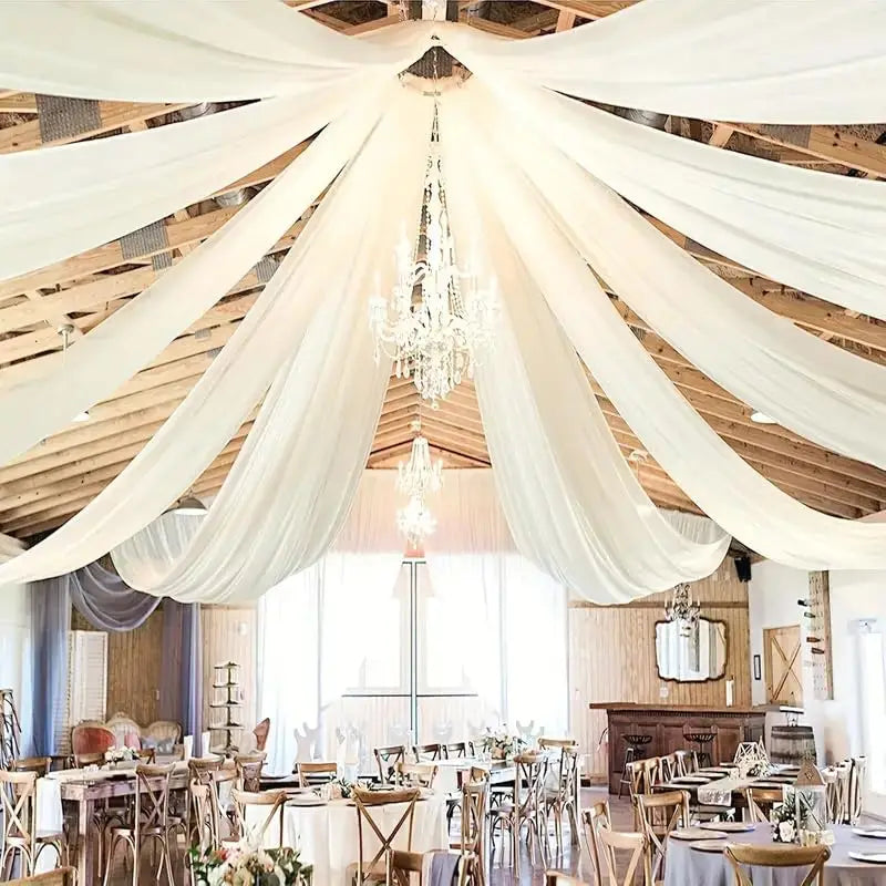 A wedding or event venue with a high ceiling draped in sheer white chiffon fabric and featuring a crystal chandelier.