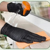 A hand wearing a black disposable nitrile glove is using an orange tool to apply product onto an orange cloth.