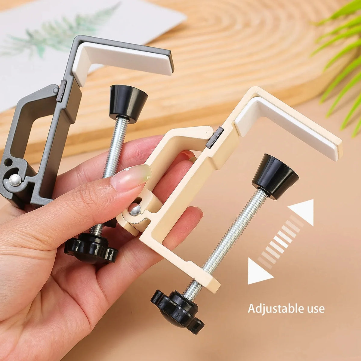 A hand holds an adjustable desk hook bag hanger with silver and black components, demonstrating its flexible use.