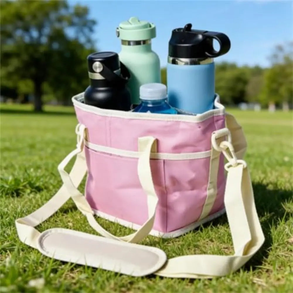 Un sac isotherme rose sur l'herbe, contenant plusieurs bouteilles d'eau réutilisables et un thermos noir.