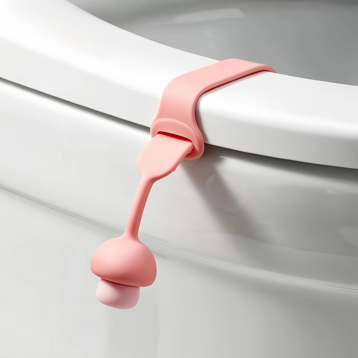 A pink silicone toilet seat lifter ring opener is shown attached to a white porcelain toilet rim.