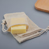 A yellow bar of soap is wrapped in a beige natural cotton mesh pouch with twine.