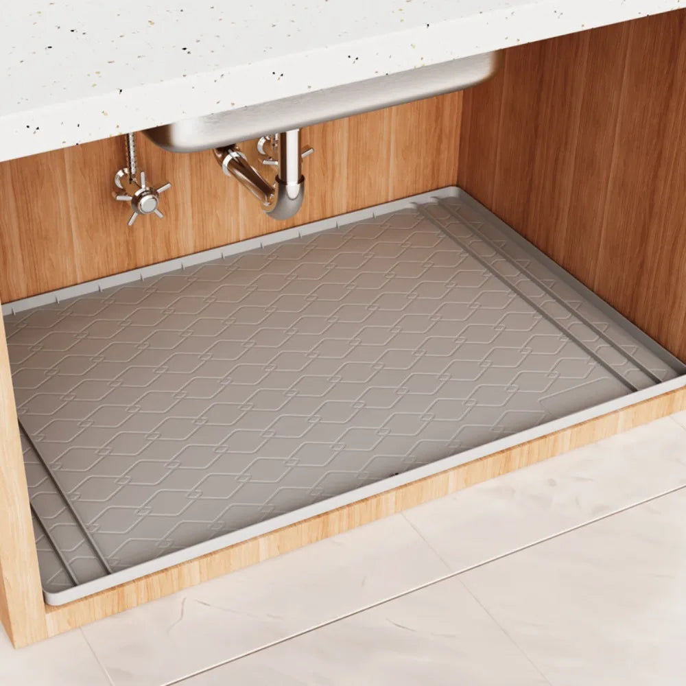 A silicone under sink waterproof mat is installed in a wooden cabinet below a white countertop.