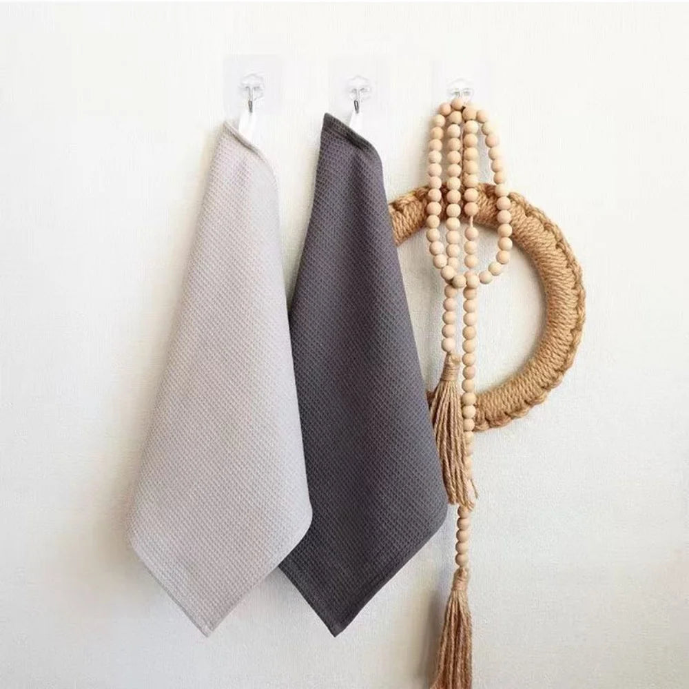 A set of three gray towels and a natural fiber broom made of woven plant material hanging on a white wall.