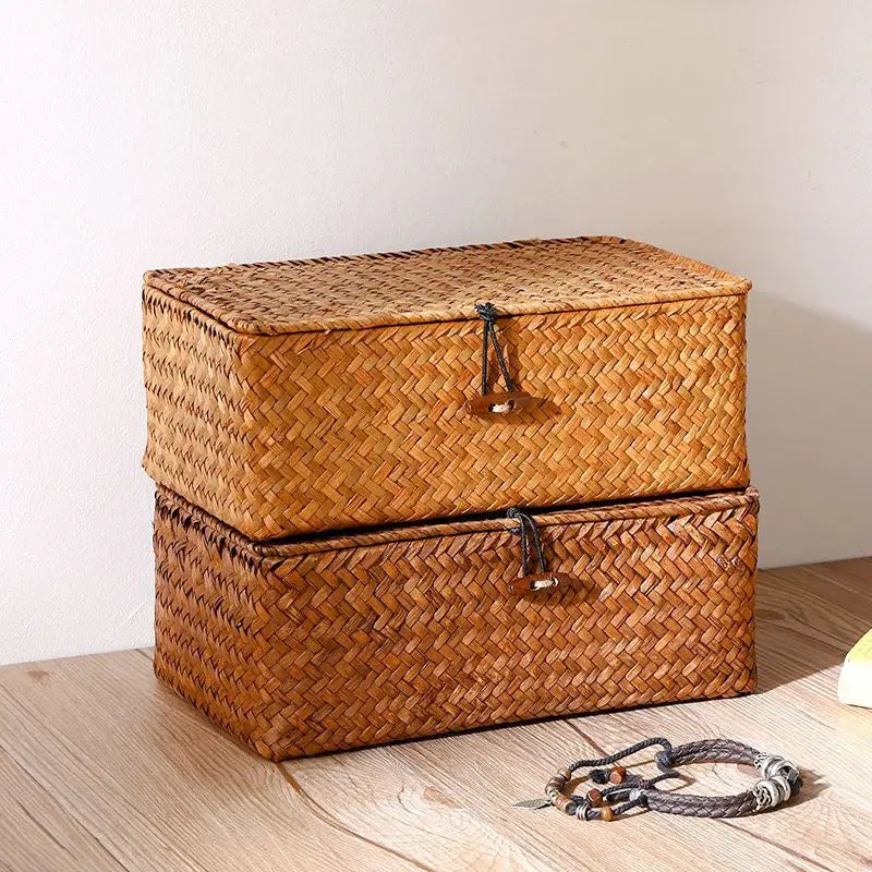 A rectangular handwoven rattan storage basket with a lid, made of natural brown fibers, resting on a wooden surface.
