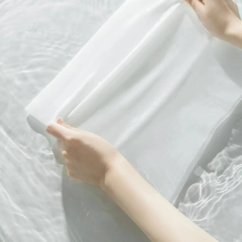 A hand is gently pressing a white disposable compressed washcloth onto the surface of water.