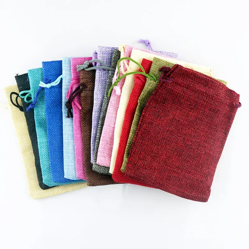 Eine Sammlung handgemachter Jute- und Leinen-Geschenktüten in verschiedenen Farben, darunter Blau, Grün, Pink, Lila und Rot.