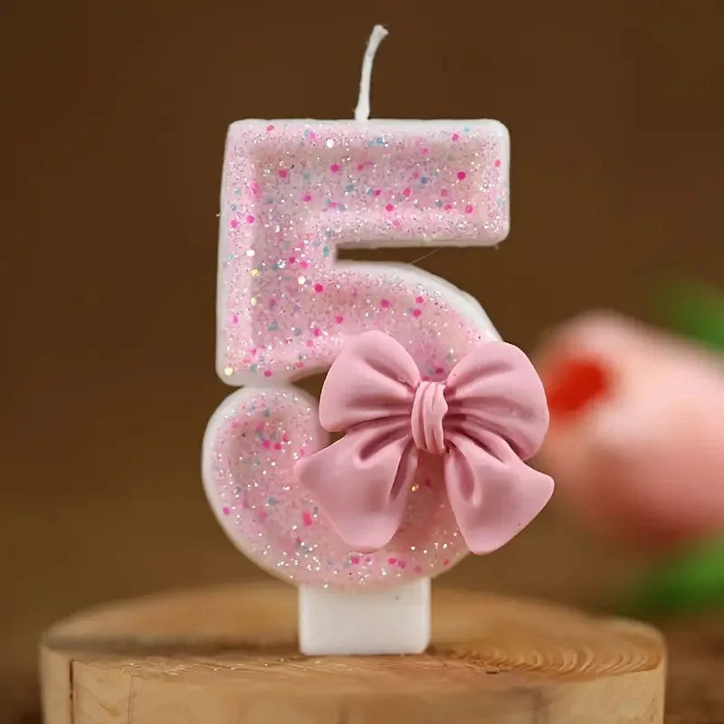 Pink glitter number candles shaped like 5 and 5 with a pink bow on a wooden surface