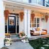 An entryway featuring a white door and porch decorated with artificial flower garlands and potted plants.