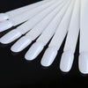 A set of white nail art practice false tips arranged in a row on a dark surface.