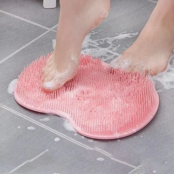 A pink silicone foot massage shower mat is placed on a gray tiled floor with water droplets.