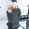 A black coffin-shaped makeup brush holder with a spider web design filled with various makeup brushes.