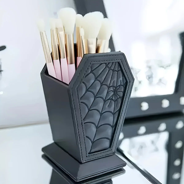A black coffin-shaped makeup brush holder with a spider web design filled with various makeup brushes.