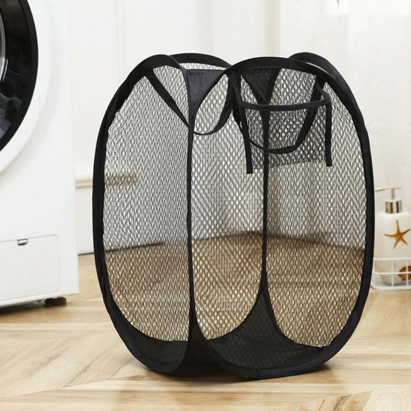 Black collapsible mesh laundry basket with side pockets sitting on a wooden floor.