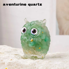 A translucent green aventurine quartz crystal shaped like an owl with large eyes resting on a white surface.