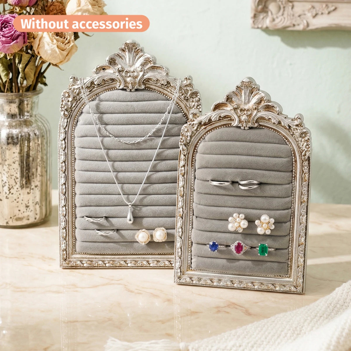 Présentoir de bijoux à cadre argenté avec panneaux de tissu gris et accents floraux décoratifs.