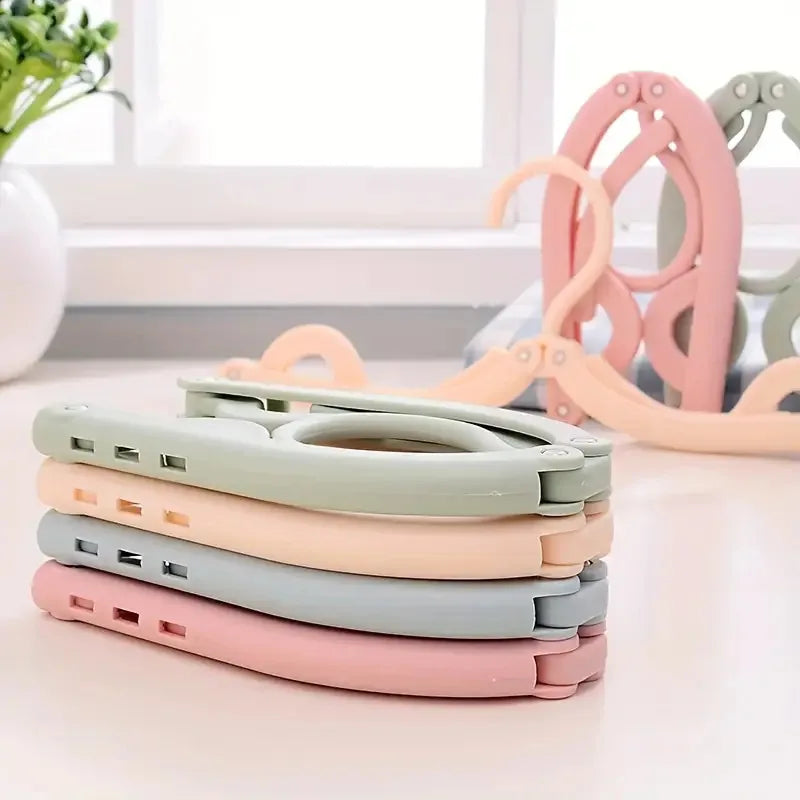A stack of pink, beige, and green portable foldable clothes hangers with pink and green wooden hangers in the background.